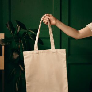 Simple cotton tote bag held by a hand against a green background, ideal for eco themes.
